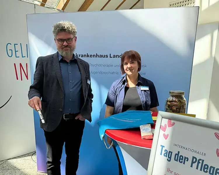 Eine Frau und ein Mann stehen an einem Infostand beim Tag der Pflege und blicken in die Kamera.