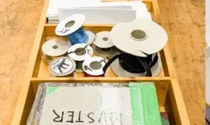 Arbeitskiste mit Spulen, Bändern und Buchbinde‑Material auf einem Werktisch – Symbolbild für Arbeitstherapie.
