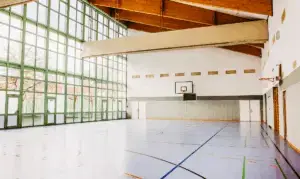 Helle Sporthalle mit großer Fensterfront, markiertem Hallenboden und Basketballkörben – Symbolbild für Bewegungstherapie.