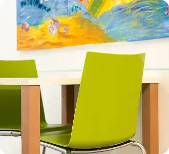 2 grüne Stühle und ein Tisch, über dem Tisch hängt ein buntes selbstgemahltes Wandbild