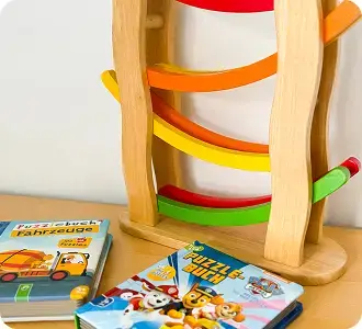 Holzspielbahn mit bunten Schienen und zwei Kinderbüchern auf dem Tisch.