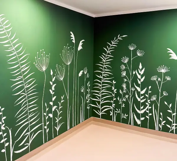 Ecke eines Raumes, mit grünen Wänden auf denen weiße Pflanzen gemalt sind